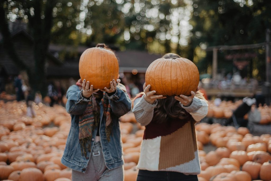 Two people holding up pumpkins surrounded by pumpkins in a field